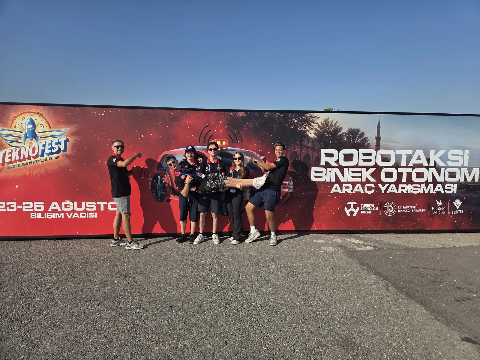 Robotaxi team in front of the TEKNOFEST autonomous vehicle competition banner at Bilişim Vadisi